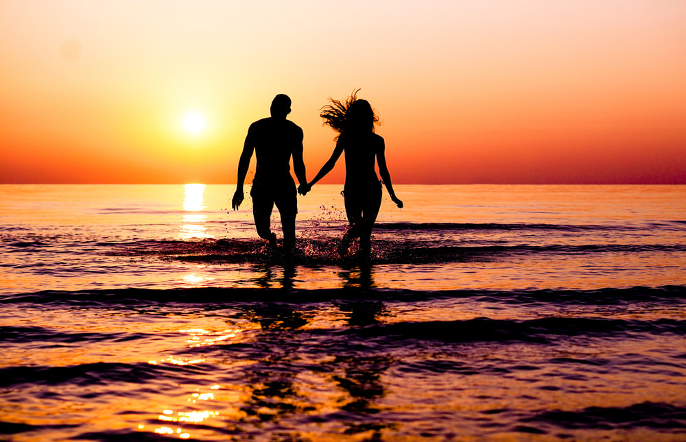 Couple running into the ocean at sunset.